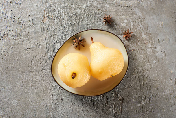 top view of delicious pear in wine served with anise on plate on grey concrete surface - Zdjęcie, obraz
