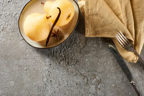 top view of delicious pear in wine served with anise on plate near cutlery and napkin on grey concrete surface - Photo, Image