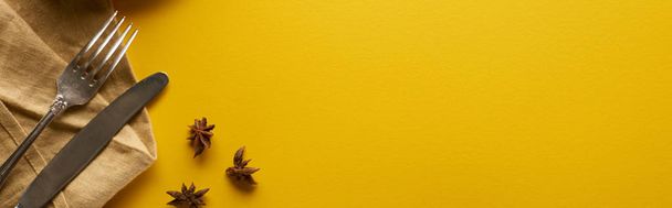 vista dall'alto di anice vicino a posate su tovagliolo beige su sfondo giallo, colpo panoramico
 - Foto, immagini