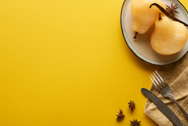 vista superior de la deliciosa pera en vino con anís en el plato cerca de cubiertos y servilleta sobre fondo amarillo
 - Foto, imagen