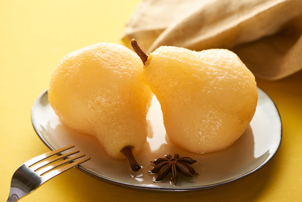 selective focus of delicious pear in wine on plate with anise near napkin and fork on yellow background - Photo, Image