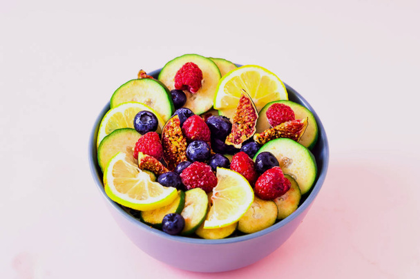 Fruitsalade van wilde bessen en exotische vruchten op roze achtergrond. Het concept van een gezond dieet, geen afval. Sluiten. - Foto, afbeelding