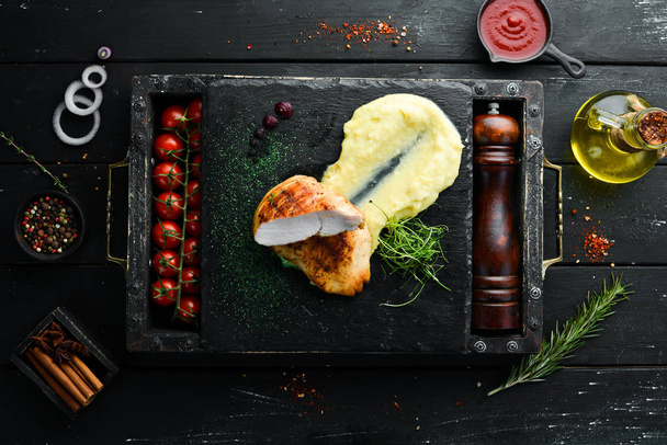 Baked chicken fillet with mashed potatoes on a black stone plate. Top view, free space for your text. Rustic style. - Valokuva, kuva