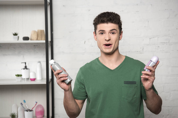 excited young man in green t-shirt looking at camera while holding deodorants - Фото, изображение