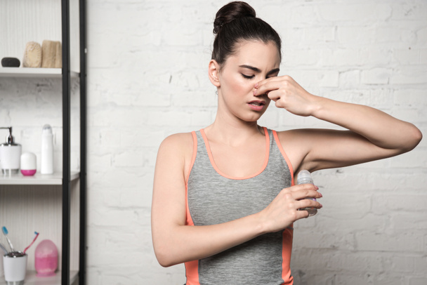 ontevreden vrouw pluggen neus met de hand tijdens het aanbrengen van deodorant op de onderarm - Foto, afbeelding