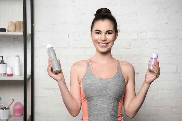 mujer alegre sonriendo a la cámara mientras sostiene desodorantes
 - Foto, imagen