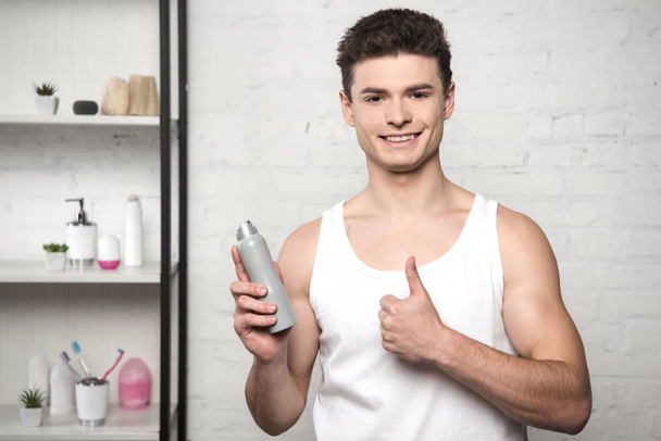 hombre sonriente con camisa blanca sin mangas mostrando el pulgar hacia arriba mientras sostiene el desodorante
 - Foto, imagen