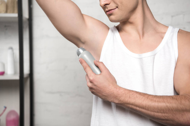 vista recortada de un joven con camisa blanca sin mangas aplicando desodorante en la axila
  - Foto, imagen