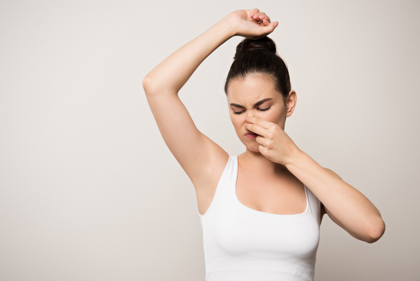 displeased woman plugging nose with hand while looking at underarm isolated on grey - Photo, image