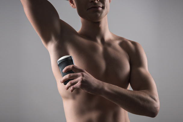 vista recortada del hombre sin camisa que sostiene el desodorante cerca de la axila aislada en gris
 - Foto, imagen