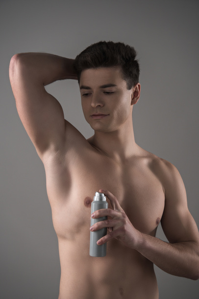jovem homem sem camisa segurando desodorizante perto da axila isolado em cinza
 - Foto, Imagem