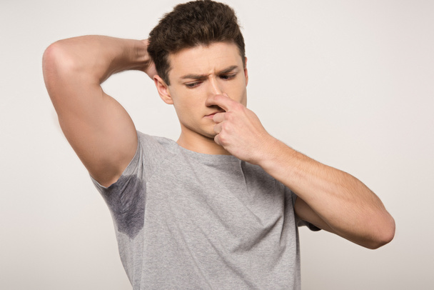 elégedetlen férfi szürke pólóban izzadt hónalj dugulás orr kézzel elszigetelt szürke - Fotó, kép