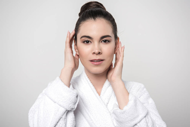 beautiful woman in bathrobe touching face while looking at camera isolated on grey - Fotoğraf, Görsel