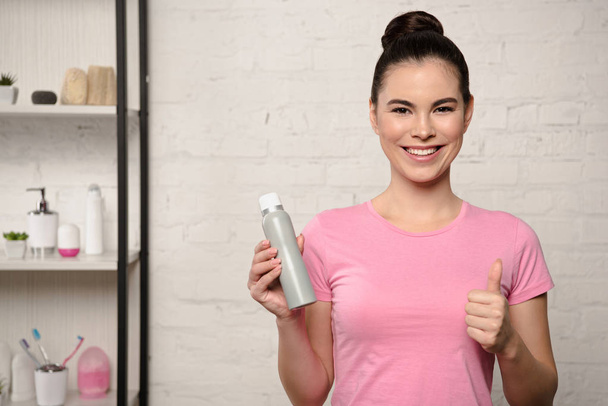 cheerful woman smiling at camera and showing thumb up while holding deodorant - Valokuva, kuva