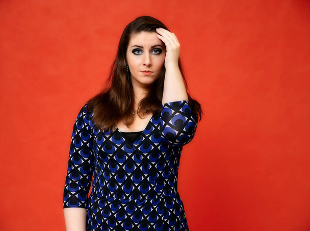 Portrait of a pretty brunette woman with a beautiful hairstyle and with excellent makeup in a dark blue blouse on a red background. He stands with a smile and shows his hands with emotions. - Foto, imagen
