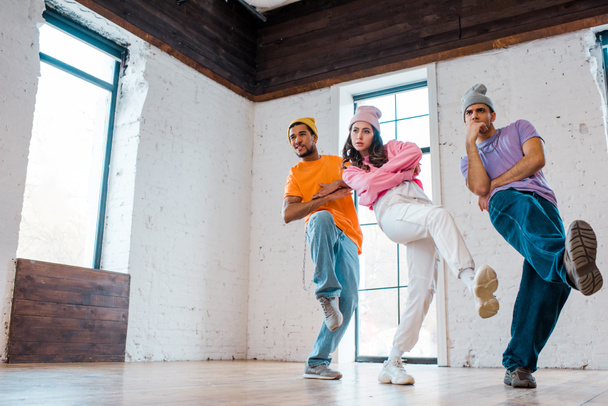 stylish girl with crossed arms breakdancing with multicultural men in hats  - Photo, Image
