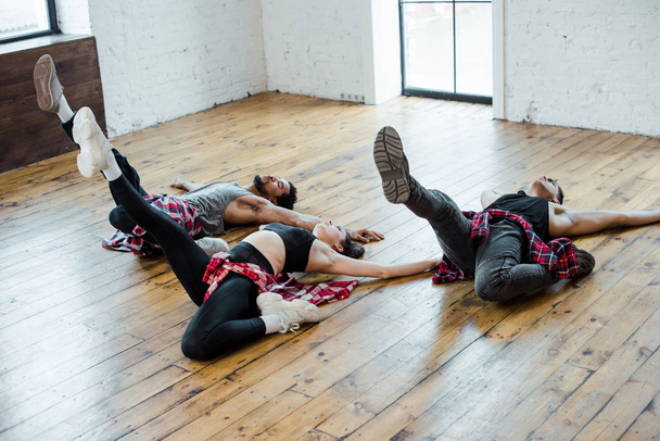 πολυπολιτισμικοί άνδρες και ελκυστική γυναίκα ξαπλωμένη στο πάτωμα, ενώ χορεύουν τζαζ funk  - Φωτογραφία, εικόνα