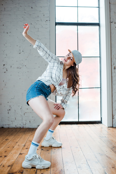 young woman in denim shorts and cap dancing hip-hop  - 写真・画像