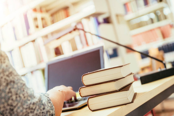 Blonde female student is sitting at the desk with pile of books, university library - 写真・画像