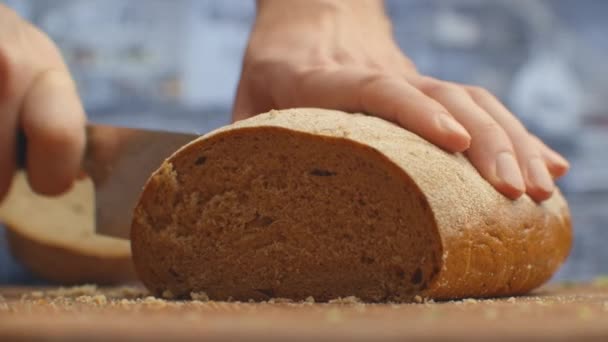 Snijd brood met een mes op een houten plank van dichtbij in de keuken. versnippering. - Video