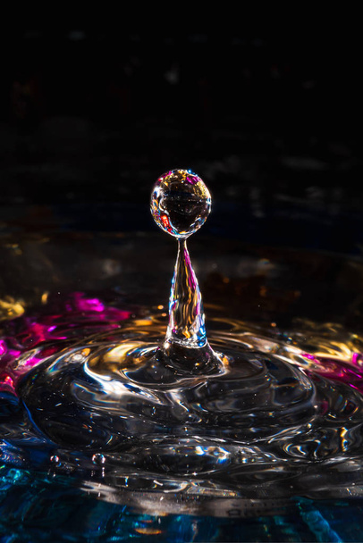 water drops splash forming ripples and waves and abstract water columns in a colorful background - 写真・画像