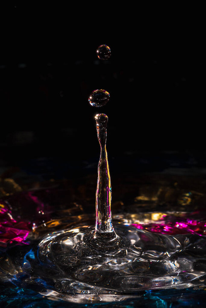 water drops splash forming ripples and waves and abstract water columns in a colorful background - Foto, afbeelding