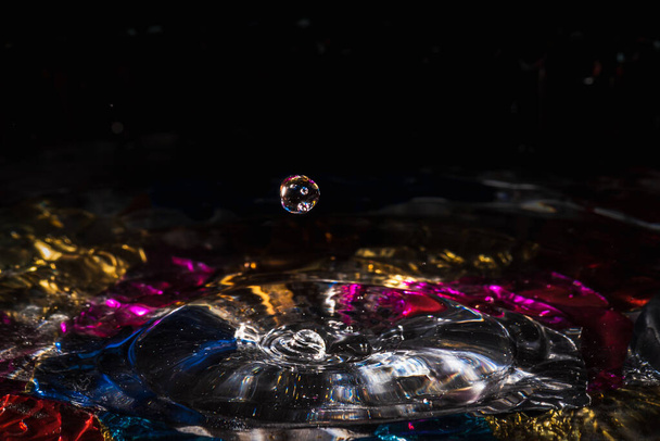 σταγόνες νερού πιτσιλίζουν σχηματίζοντας κυματισμούς και κύματα και αφηρημένες κολώνες νερού σε ένα πολύχρωμο φόντο - Φωτογραφία, εικόνα