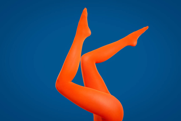 Woman wearing orange tights on blue background, closeup of legs - Foto, afbeelding
