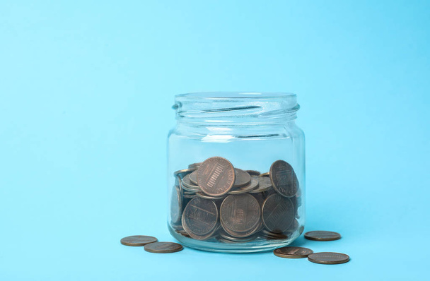Glass jar with coins on light blue background - Zdjęcie, obraz