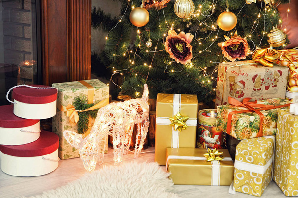 Golden Christmas gifts and deer near Christmas fir-tree taken cl - Foto, imagen
