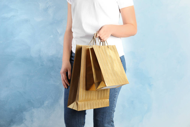 Woman with gold shopping paper bags on light blue background, closeup - Fotó, kép