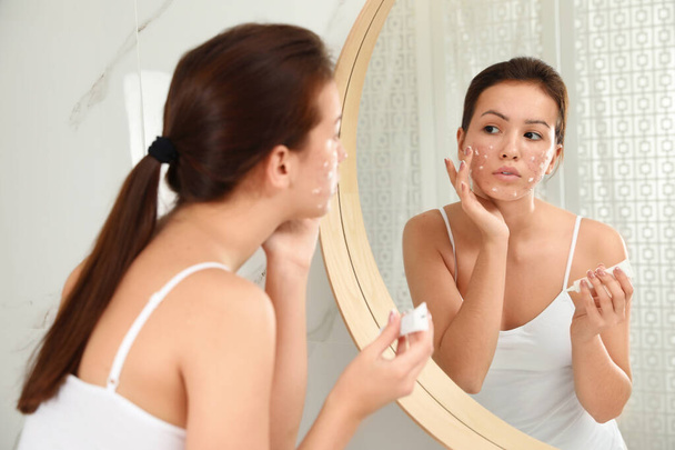 Teen girl with acne problem applying cream near mirror in bathro - Zdjęcie, obraz