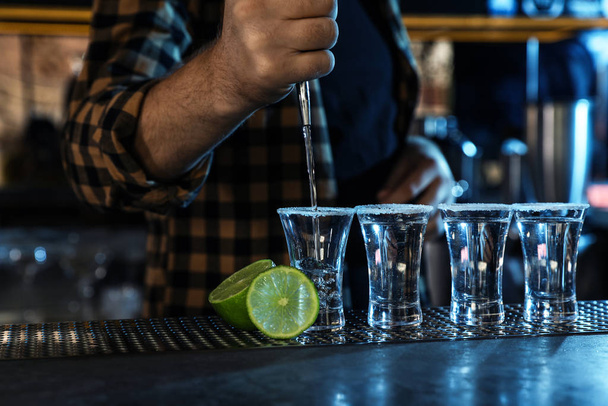 Bartender pouring Mexican Tequila into shot glasses at bar counter, closeup - Fotó, kép