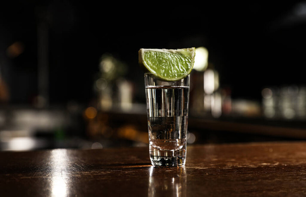 Mexican Tequila shot with lime slice on wooden bar counter - Photo, image