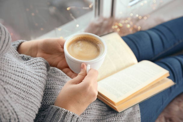 Γυναίκα με φλιτζάνι καφέ βιβλίο ανάγνωσης στο σπίτι, closeup - Φωτογραφία, εικόνα