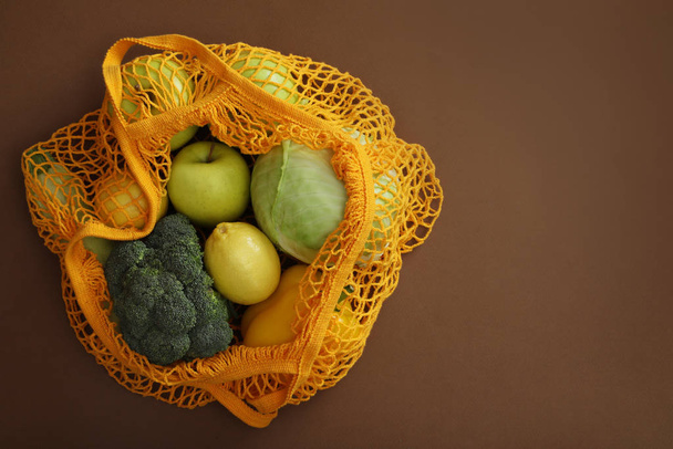Net bag with fruits and vegetables on brown background, top view - Φωτογραφία, εικόνα