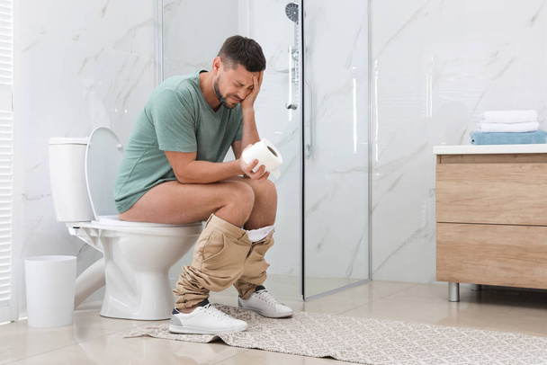 Man suffering from hemorrhoid on toilet bowl in rest room - 写真・画像