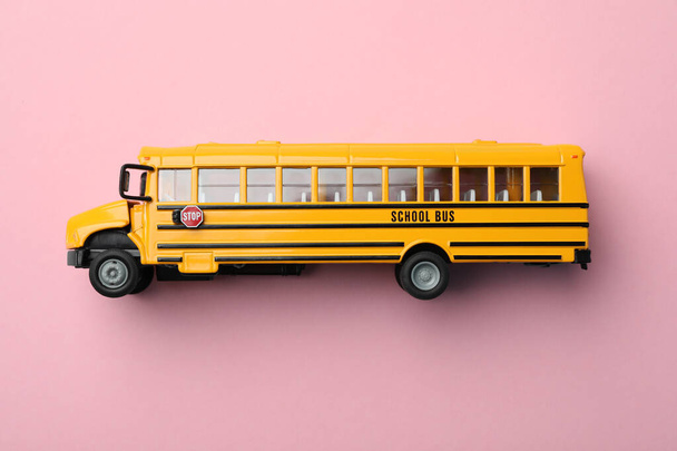 Yellow school bus on pink background, top view. Transport for students - Φωτογραφία, εικόνα