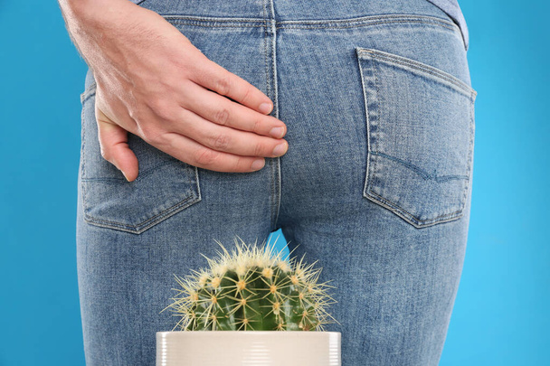 Man sitting down on cactus against light blue background, closeup. Hemorrhoid concept - 写真・画像
