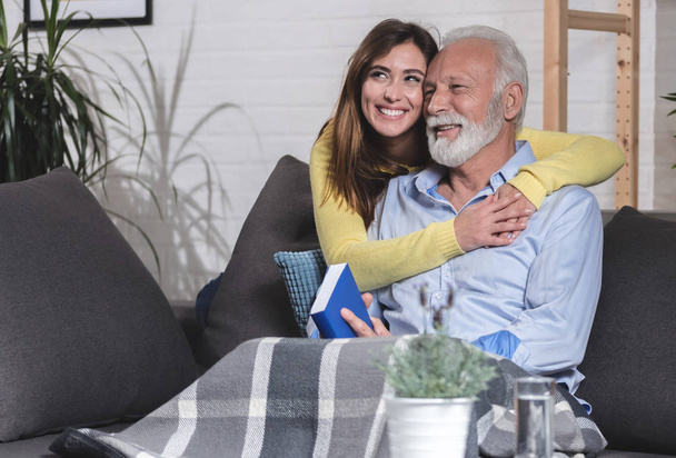 Titelbild Enkelin umarmt ihren Großvater auf der Couch sitzend - Foto, Bild