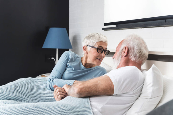 Romantic senior couple laughing while lying in bed at home - Fotoğraf, Görsel