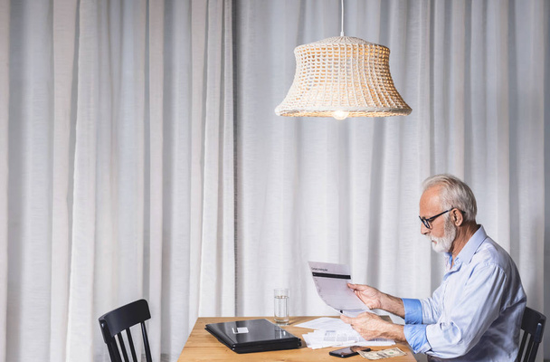 Imaginary retiree reading an electricity bill. Concept of salary, people, calculations, interest and pension payment. Copy space image - Fotografie, Obrázek