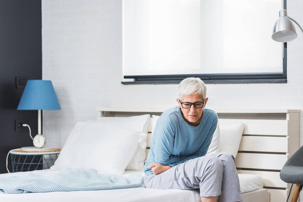 Senior woman suffering from stomach ache after sleep at home in bed, menopause concept - Foto, afbeelding