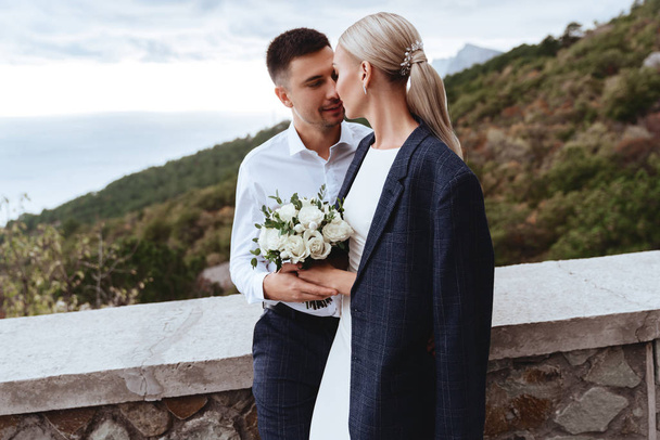 Young newly wed couple, bride and groom kissing, hugging on perfect view of mountains - Φωτογραφία, εικόνα