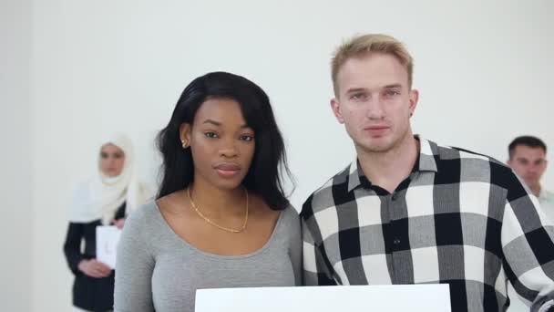 Serious young african american woman and european man holding in their hands inscription "No racism" in front muslim woman in hijab and another european guy with written words"Love.Happiness" - Video, Çekim