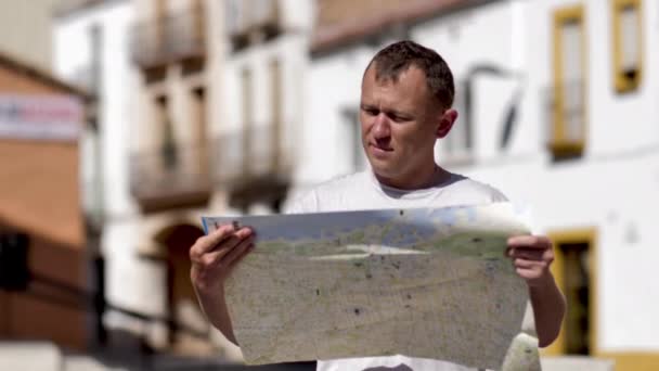 Traveler man holds a city map in his hands, stands on the street and examines a map - 映像、動画