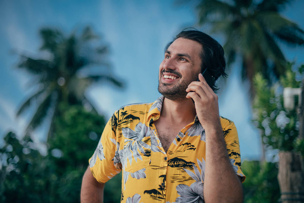 Ein zufriedener Mann steht mit einem Handy in der Hand auf einem Palmenhintergrund - Foto, Bild
