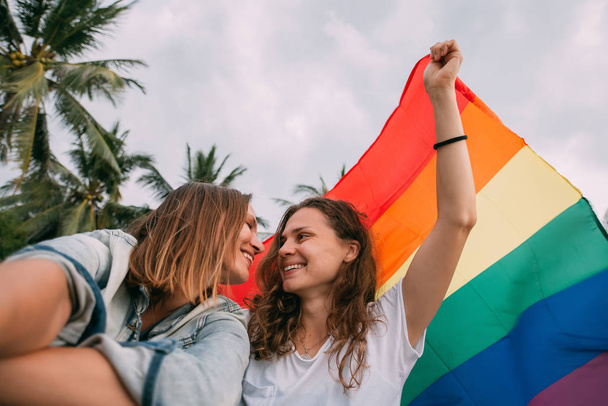 Two women with rainbow flag on the beach on a background of palm trees - Foto, immagini