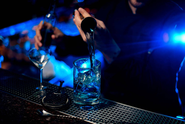 Profesyonel barmen mavi bir alkollü likör dolduruyor jigger 'dan mavi ışık altında bir ölçü kabına - Fotoğraf, Görsel