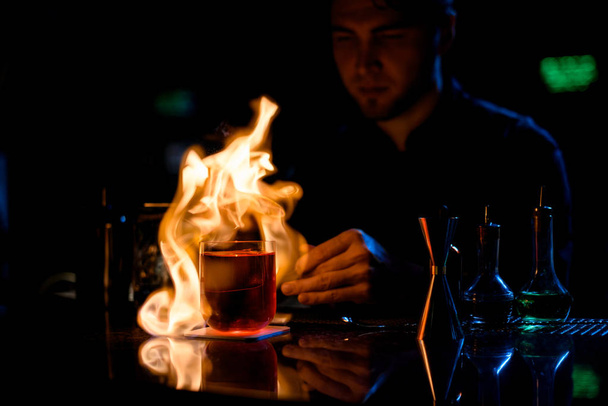 Cantinero profesional que sirve el cóctel alcohólico rojo con fuego de hielo la rodaja de limón en pinzas
 - Foto, imagen